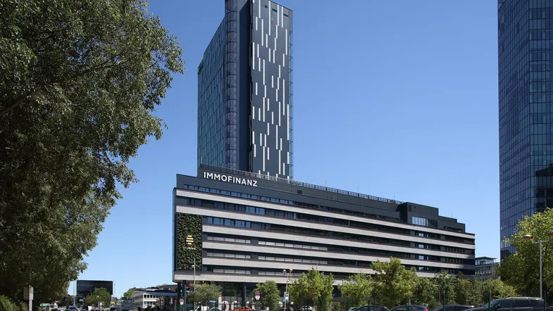 Modernes Hochhaus mit Glasfassade und begrüntem Sockelgebäude an einer belebten Straße.