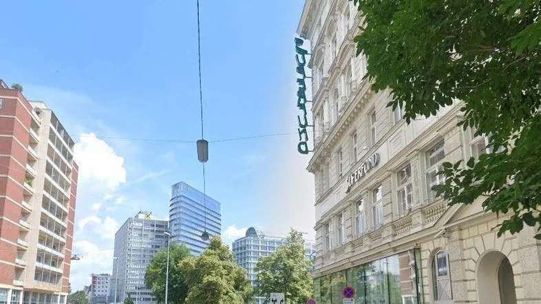 Blick auf eine belebte Stadtstraße mit historischen und modernen Gebäuden unter blauem Himmel.