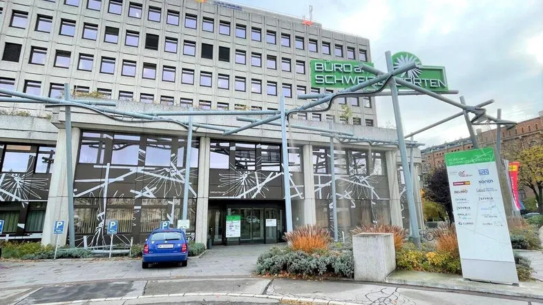 Modernes Bürogebäude mit Betonfassade, großen Fenstern und einem Eingangsbereich mit Beschilderung.