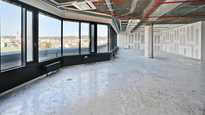 Großer, unmöblierter Büroraum mit weitem Stadtblick und sichtbaren Installationen an der Decke.