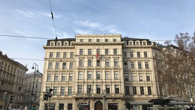Klassisches Gebäude mit historischer Fassade an einer belebten Straße in der Stadt, unter einem bewölkten Himmel.
