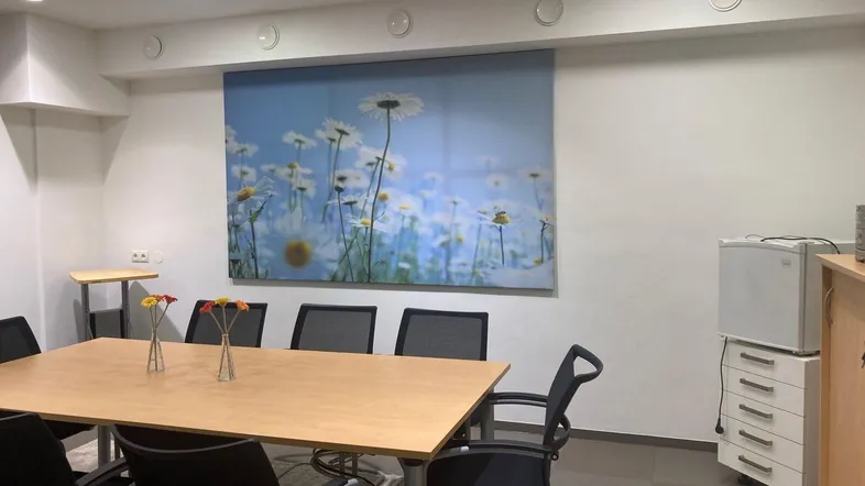 Heller Konferenzraum mit großem Holztisch, bequemen Stühlen und einem Wandbild mit Gänseblümchen.