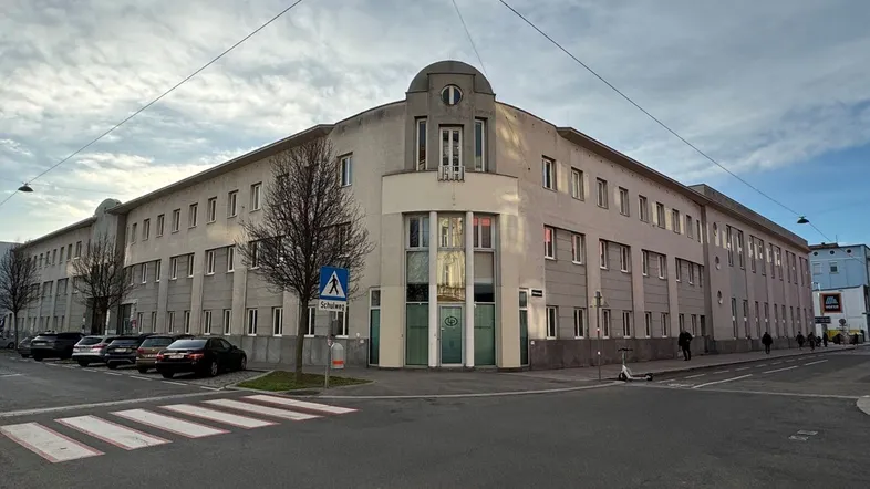 Ein großes, mehrstöckiges Gebäude mit vielen Fenstern und einer markanten, abgerundeten Ecke an einer Straßenkreuzung.