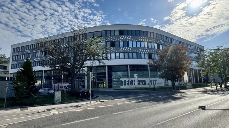 Modernes Bürogebäude mit geschwungener Glasfassade und vielen Fenstern unter blauem Himmel.