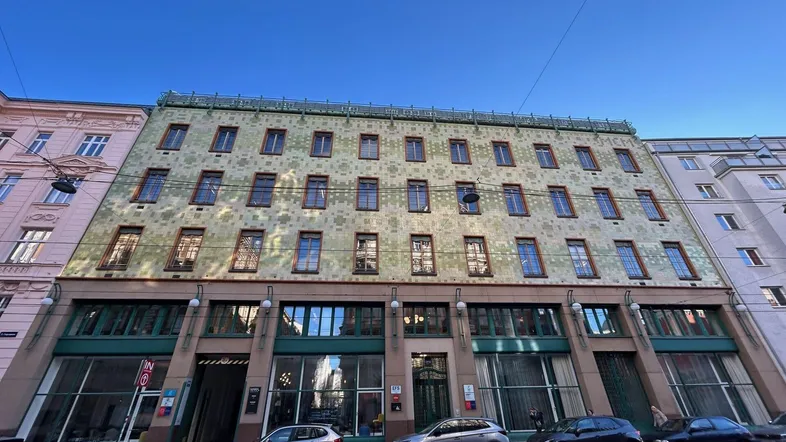 Historisches Gebäude mit einzigartiger grüner Fassade und großen Schaufenstern an einer belebten Stadtstraße.