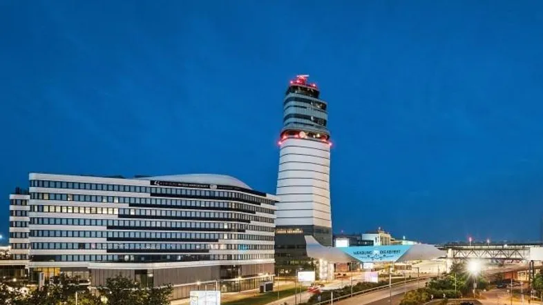 Moderne Bürogebäude und ein markanter Kontrollturm bei Dämmerung, beleuchtet vor einem dunklen Himmel.