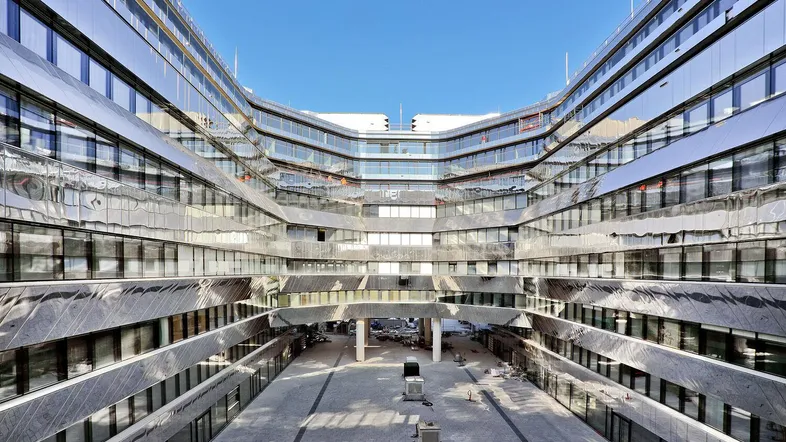 Moderne Architektur eines Bürogebäudes mit spiegelnden Fassaden und einem zentralen Innenhof unter blauem Himmel.