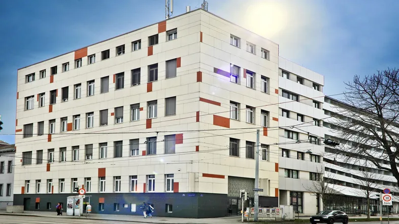 Modernes Bürogebäude mit weißer und oranger Fassade unter blauem Himmel an einer städtischen Straße.