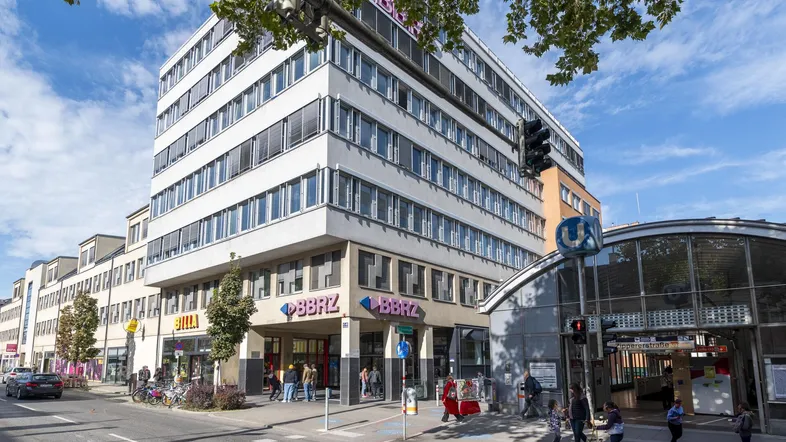 Modernes Geschäftsgebäude mit mehreren Etagen, Ladenflächen im Erdgeschoss und einer U-Bahn-Station davor.