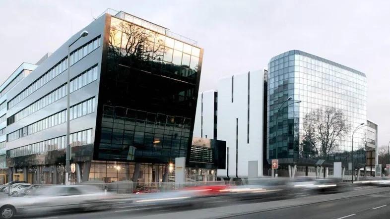 Moderne Bürogebäude mit Glasfassaden und reflektierenden Oberflächen entlang einer belebten Straße bei Dämmerung.