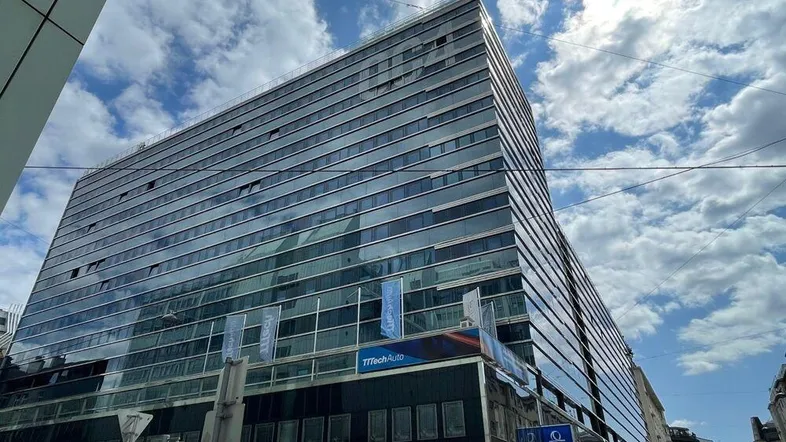Modernes Bürogebäude mit Glasfassade unter bewölktem Himmel in städtischer Umgebung.