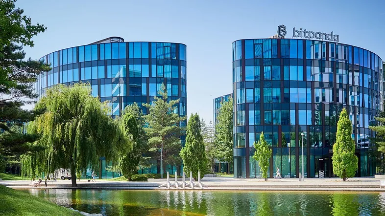 Moderne Bürogebäude mit blauer Glasfassade und umgebender Grünfläche mit Teich unter blauem Himmel.