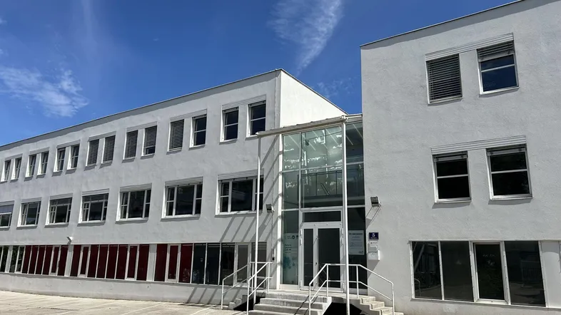 Modernes Bürogebäude mit weißer Fassade, vielen Fenstern und einem gläsernen Eingangsbereich unter blauem Himmel.