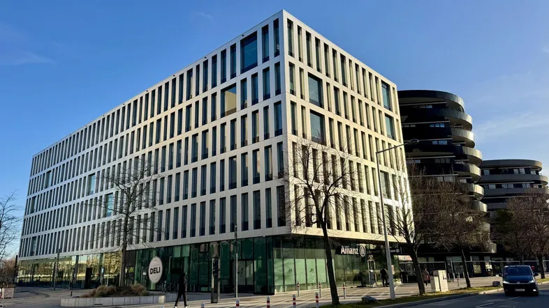 Modernes Bürogebäude mit markanter Fassade und großen Fenstern unter blauem Himmel, umgeben von städtischer Infrastruktur.