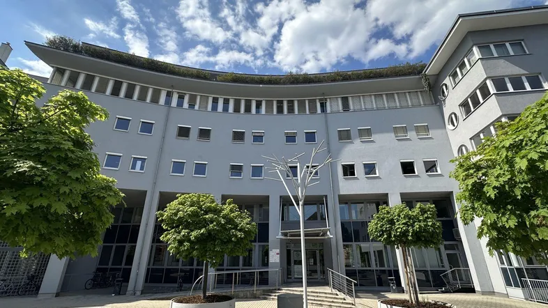 Modernes Bürogebäude mit geschwungener Fassade, begrüntem Dach und Bäumen im Eingangsbereich.