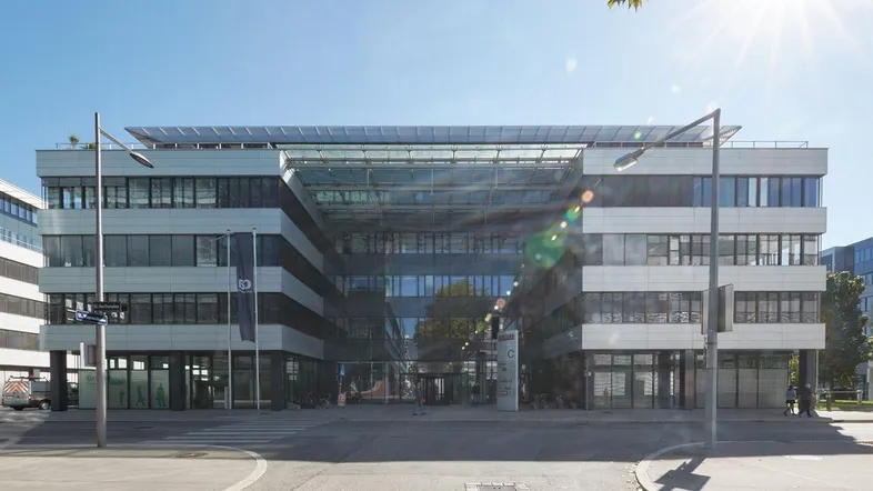 Modernes Bürogebäude mit Glasfassade und Solarpaneelen auf dem Dach unter strahlendem Sonnenschein.