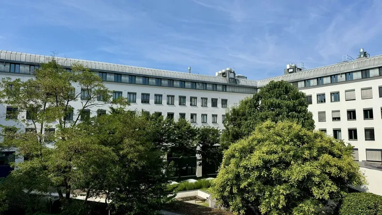 Blick auf die moderne Gebäudefassade mit einem begrünten Innenhof und klarem blauen Himmel.
