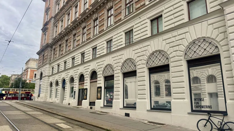 Klassisches Gebäude mit historischer Fassade und großen Bogenfenstern entlang einer Straße mit Straßenbahnschienen.