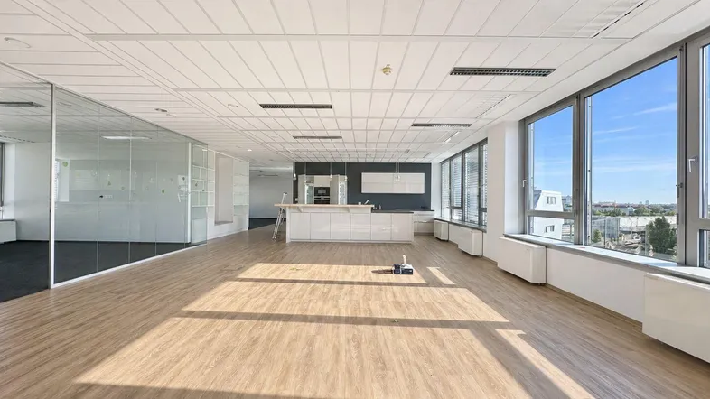 Geräumiges, helles Büro mit offener Küchenzeile, großen Fenstern und modernem Bodenbelag.