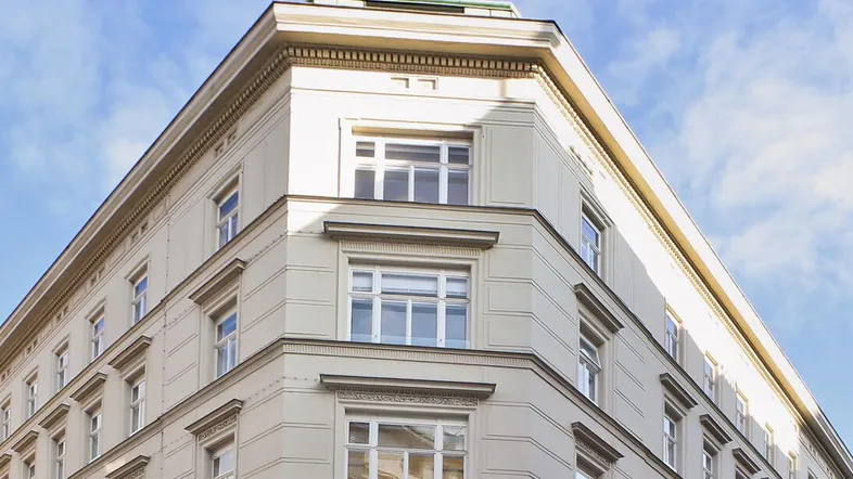 Elegante Eckfassade eines historischen Gebäudes unter blauem Himmel mit Wolken.