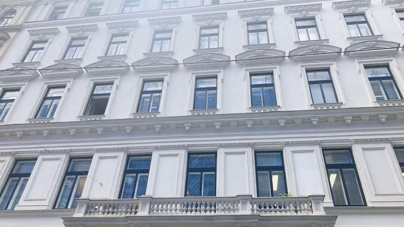 Klassische weiße Fassade eines Altbaus mit vielen Fenstern und einem kleinen Balkon.