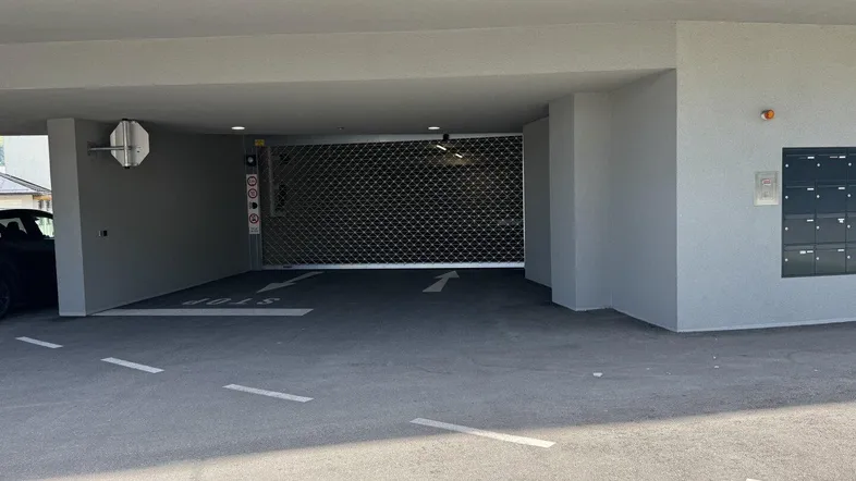 Eingangsbereich einer Tiefgarage mit geschlossenem Rolltor und Briefkästen an der Seite.