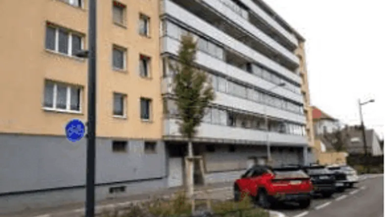 Gebäudefassade eines Mehrfamilienhauses mit Parkplätzen und Fahrradweg davor.