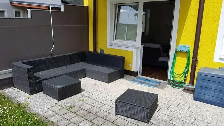 Gepflasterte Terrasse mit Rattan-Sitzgruppe und Zugang zum Innenbereich, ideal für entspannte Stunden im Freien.