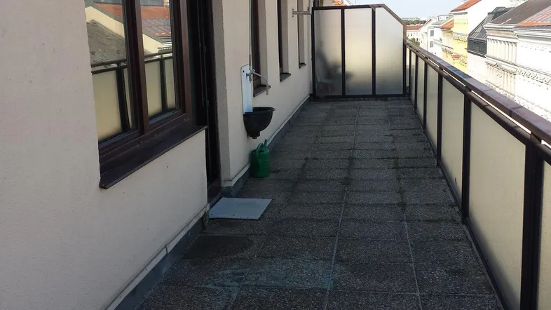 Langer Balkon mit Fliesenboden, Markise und Blick auf die umliegenden Dächer.