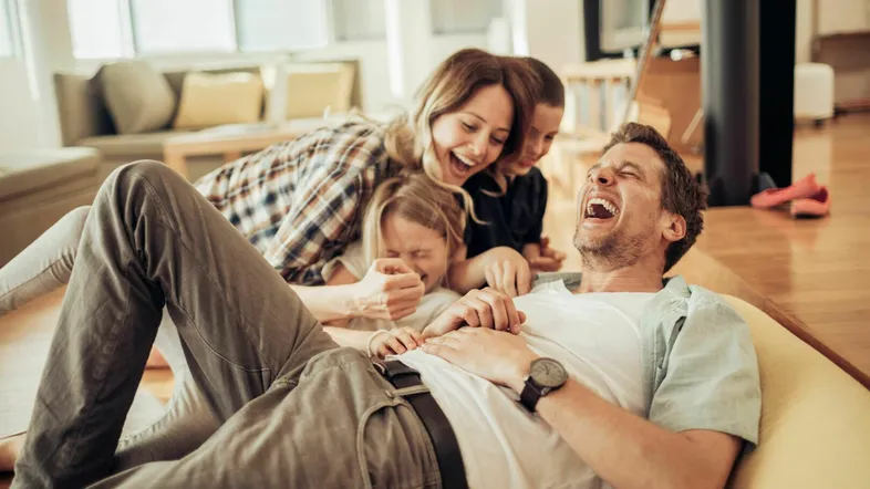 Helles Wohnzimmer mit Holzboden, in dem eine Familie lachend auf einem Sofa entspannt.