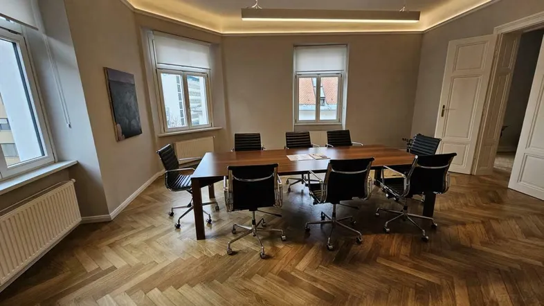 Geräumiger Konferenzraum mit großem Holztisch, bequemen Stühlen und elegantem Fischgrätparkettboden.
