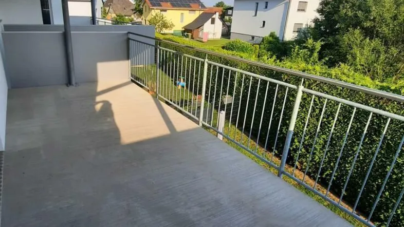 Heller Balkon mit Betonboden und Blick auf die umliegende Wohngegend und viel Grün.