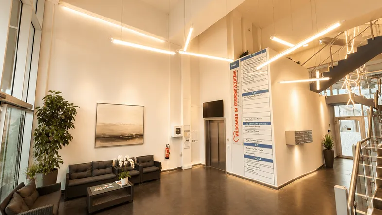 Geräumige und helle Lobby eines Gesundheitszentrums mit hohen Decken, modernen Leuchten und bequemen Sitzgelegenheiten.
