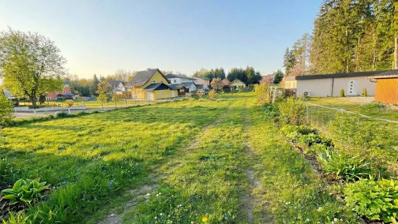 Grünes Grundstück mit Wegen und umliegenden Häusern, umgeben von Natur und Bäumen.