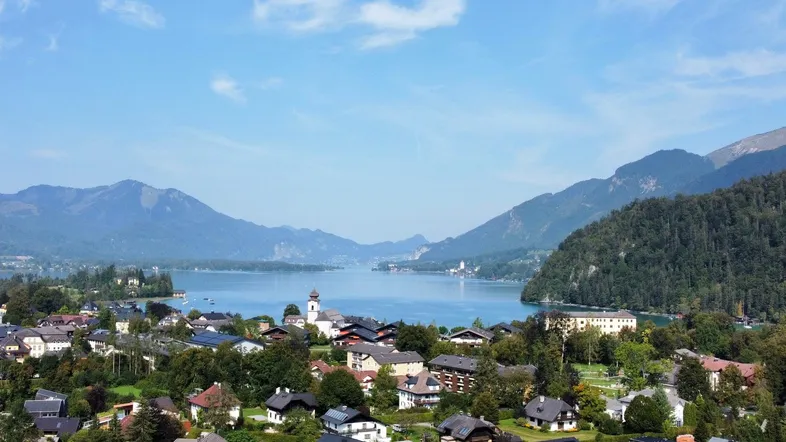 Panoramablick auf eine malerische Stadt am See, umgeben von majestätischen Bergen und grüner Landschaft.