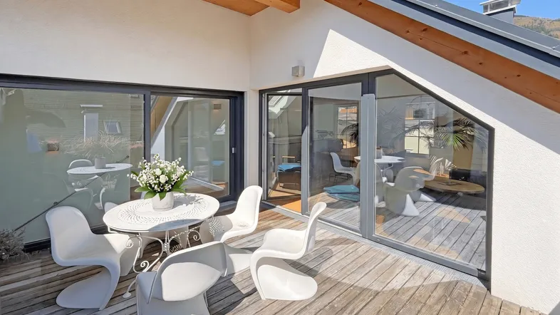 Sonnige Dachterrasse mit Holzboden, modernen Gartenmöbeln und Zugang zum Innenbereich.