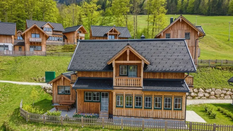 Traditionelles Holzchalet mit dunklem Dach in einer malerischen Berglandschaft, umgeben von grünen Hügeln.