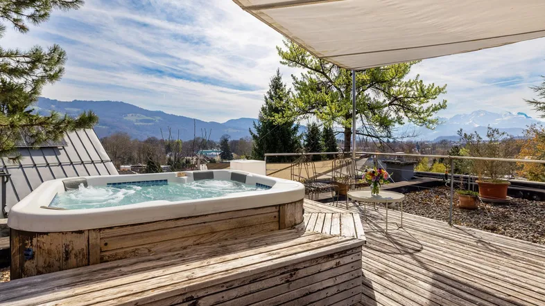 Große Holzterrasse mit Whirlpool und atemberaubendem Bergblick unter einem Sonnensegel.