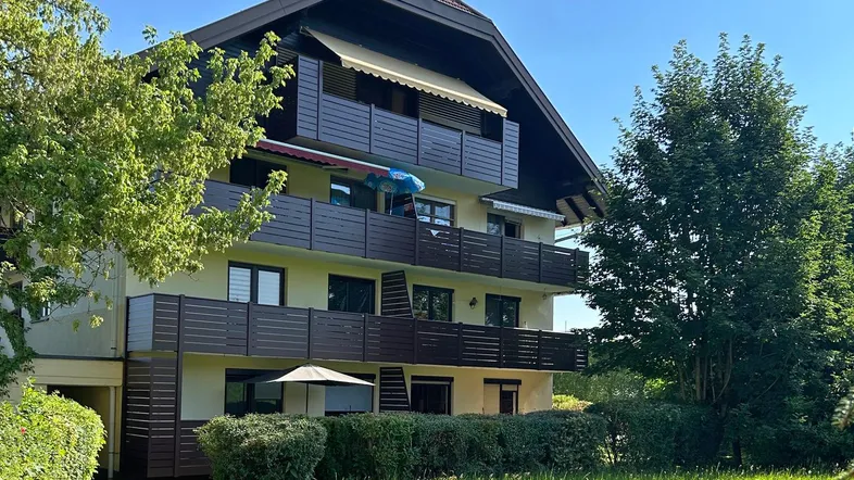 Mehrstöckiges Wohngebäude mit mehreren Balkonen und gepflegtem Vorgarten unter blauem Himmel.