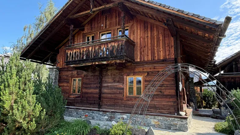 Traditionelles Holzchalet mit geschnitztem Balkon und gepflegtem Vorgarten unter blauem Himmel.
