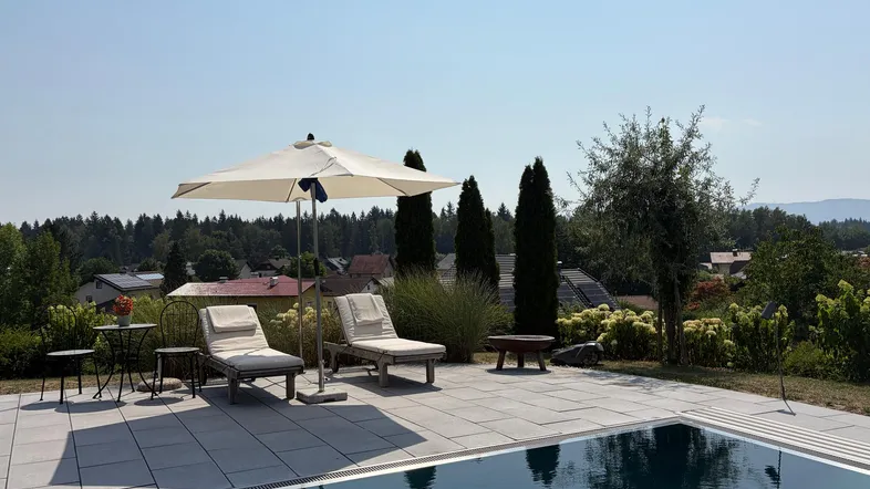 Großzügiger Außenbereich mit Pool, Liegestühlen und Sonnenschirm unter blauem Himmel.