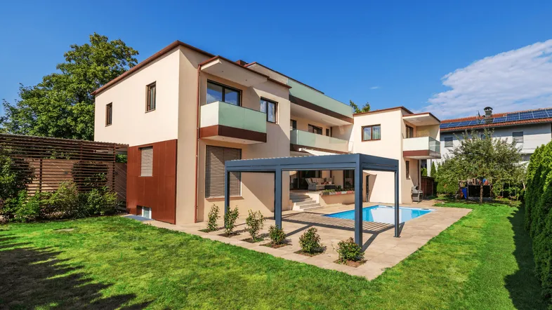 Modernes Haus mit großem Garten, Pool und Pergola unter blauem Himmel.