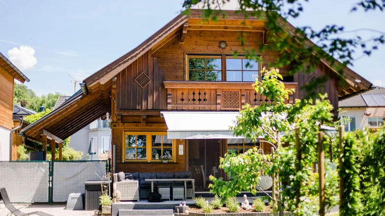 Charmantes Holzhaus mit gepflegtem Garten, Terrasse und gemütlicher Sitzecke im Freien unter blauem Himmel.