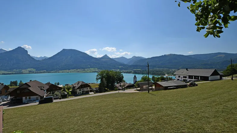 Panoramablick auf einen malerischen See, umgeben von majestätischen Bergen und einer idyllischen Siedlung.