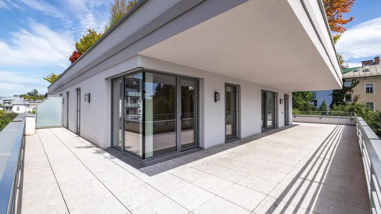 Große, helle Terrasse mit Fliesenboden und moderner Balustrade, ideal für Entspannung im Freien.
