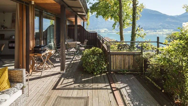 Große Holzterrasse mit Sitzgelegenheiten, Grill und malerischem Blick auf den See und die umliegenden Berge.