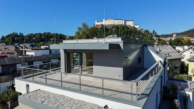 Moderne Dachterrasse mit Panoramablick auf die Stadt und die Festung Hohensalzburg unter blauem Himmel.
