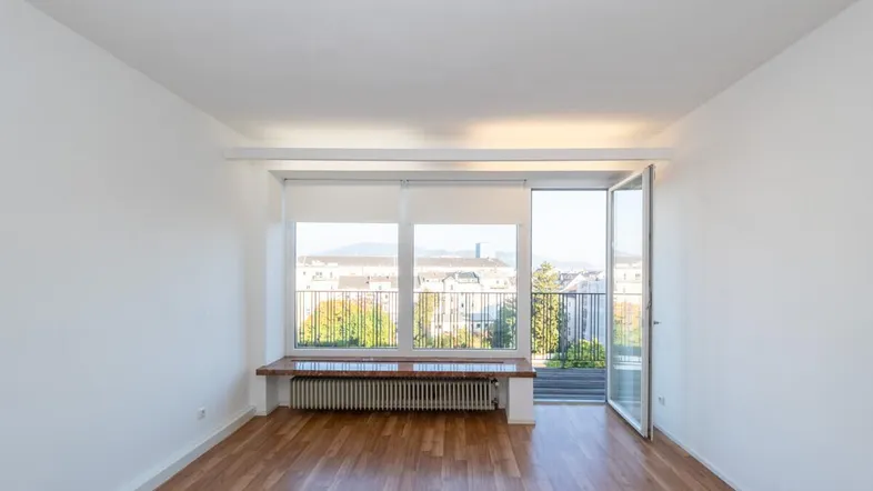 Helles Wohnzimmer mit Parkettboden, großen Fenstern und Zugang zu einem Balkon mit Stadtblick.