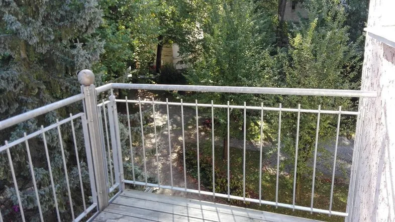Kleiner Balkon mit Metallgeländer und Holzboden, bietet einen ruhigen Blick ins Grüne.