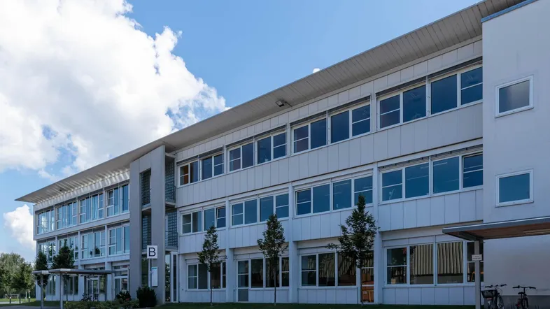 Modernes Bürogebäude mit vielen Fenstern und Parkplätzen unter blauem Himmel.